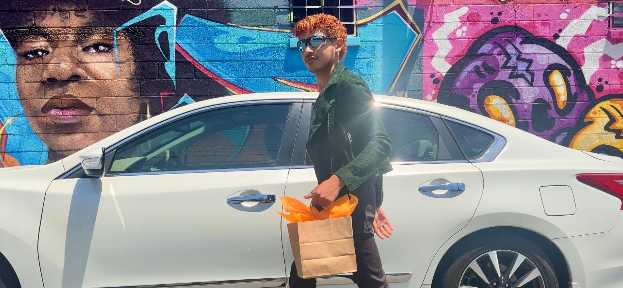 Person standing next to a white car with colorful graffiti in the background